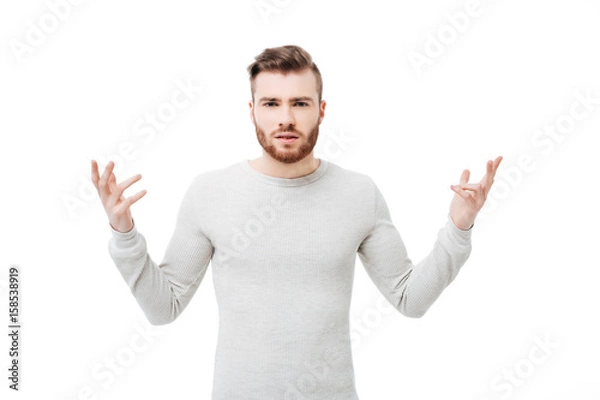 Fototapeta Embarrassed and confused young man showing why hand gesture over white background