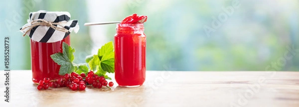 Obraz Fresh homemade red currant jam in jar with fresh picked currants on table against light bokeh background. Horizontal close-up with space for text.