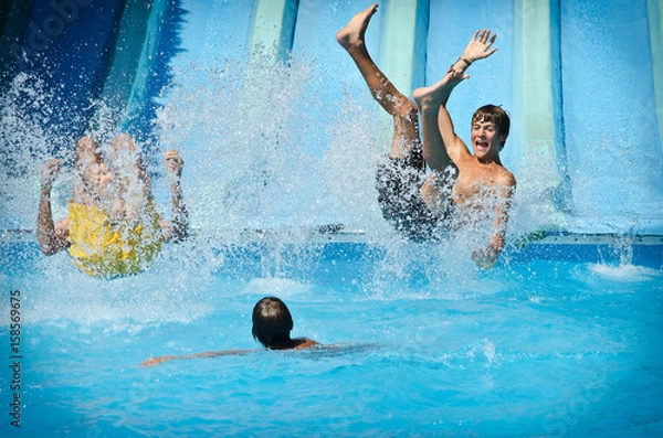 Fototapeta Młodzi ludzie bawią się na zjeżdżalniach w aquaparku, pluskają się w basenie