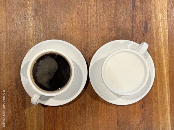 Fototapeta One cup of black coffee and one cup of white milk, placed side by side on a wooden table.