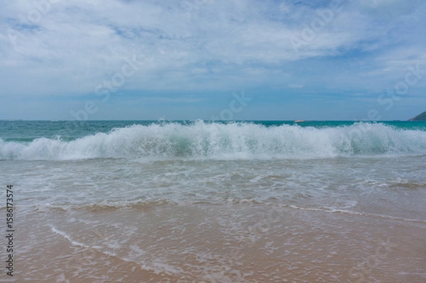 Fototapeta Seascape on waves with foam and spray, sky and beach. Ocean waves crashing on a sandy beach
