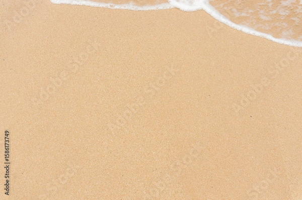 Fototapeta Soft wave on the sandy beach, background. View from the top of the sandy beach and foam from the wave.