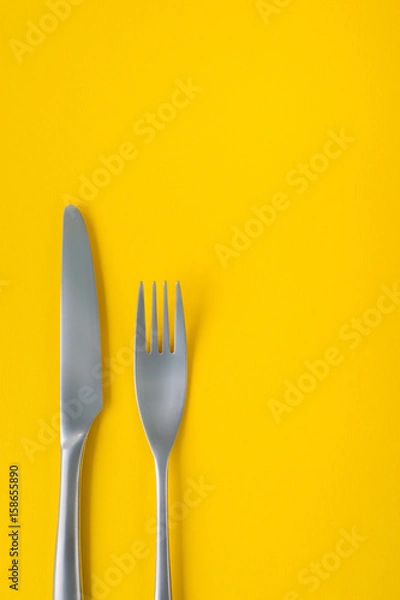 Fototapeta Fork and knife on yellow background, sparse composition with copy space.