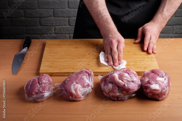 Fototapeta man in the apron wipe cloth cutting Board on a background of packaged meat in plastic bags