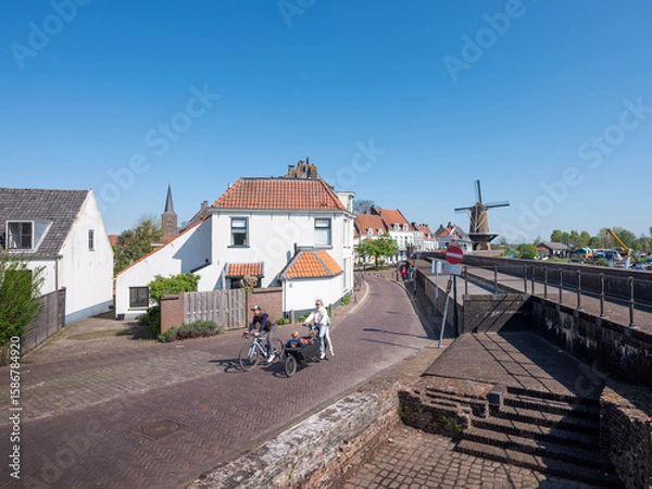 Fototapeta bicycles and street with old houses and windmill in dutch town of wijk bij duurstede on sunny day in spring