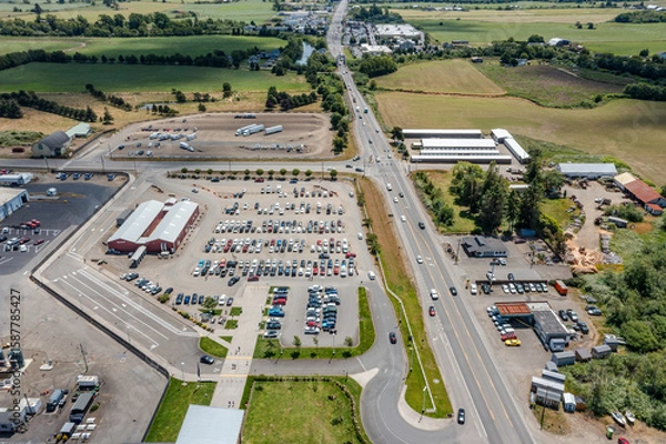 Fototapeta Aerial drone top-down view of a busy and full parking lot at a large dairy factory in Tillamook, Oregon, with many parked cars and highway 101 visible	
