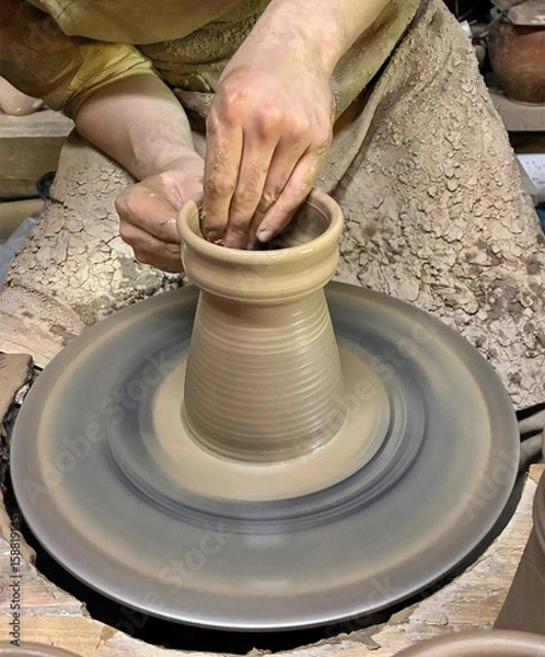Obraz Closeup of clay product being made on pottery wheel. Hands of young craftsman forming clay pot on pottery wheel. Hobbies and creativity.