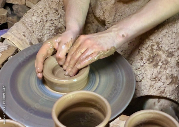 Obraz Hands of young potter working with clay and making vase or pot, jug or mug. Throwing pottery on wheel closeup.