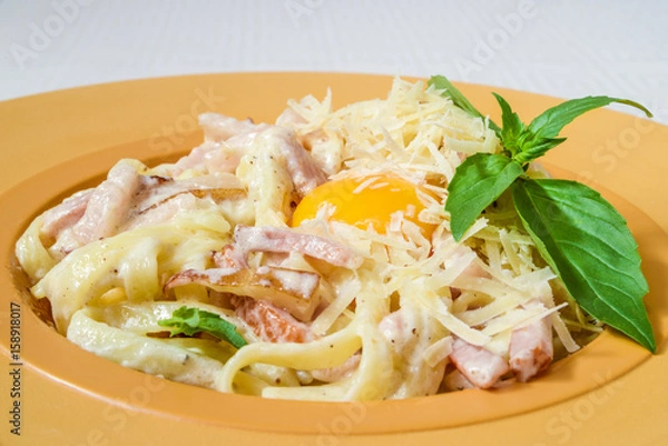 Fototapeta Tasty pasta with cheese, bacon, egg and herbs, on a yellow plate. Horizontal frame