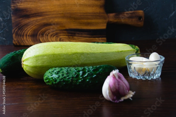 Fototapeta Green vegetables on a dark background. Cucumbers, garlic and zucchini on a wooden table. Concept of cooking healthy food and healthy eating