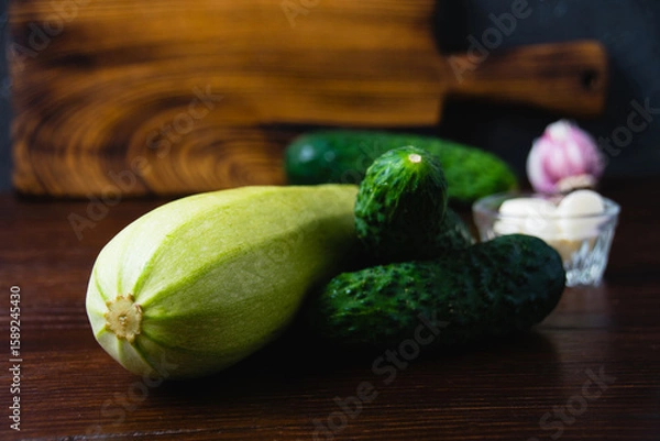 Fototapeta Green vegetables on a dark background. Cucumbers, garlic and zucchini on a wooden table. Concept of cooking healthy food and healthy eating