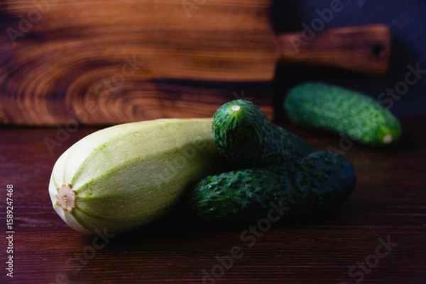 Fototapeta Green vegetables on a dark background. Cucumbers and zucchini on a wooden table. Concept of cooking healthy food and healthy eating.