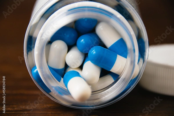 Fototapeta White and blue pills in a jar, macro on a dark wooden background. Self-medication concept.