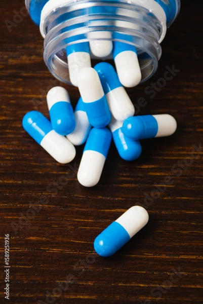 Fototapeta White and blue pills in a jar, macro on a dark wooden background. Self-medication concept.