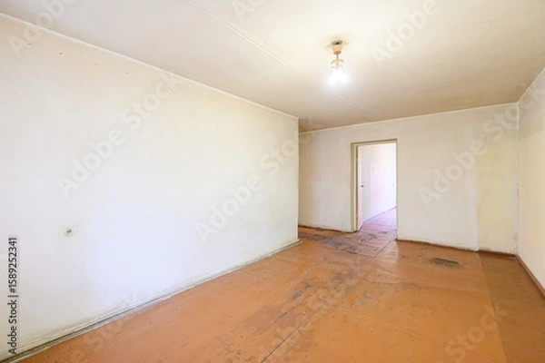 Fototapeta empty room with beige walls, a worn wooden floor, and a simple light fixture. An open doorway leads to another room