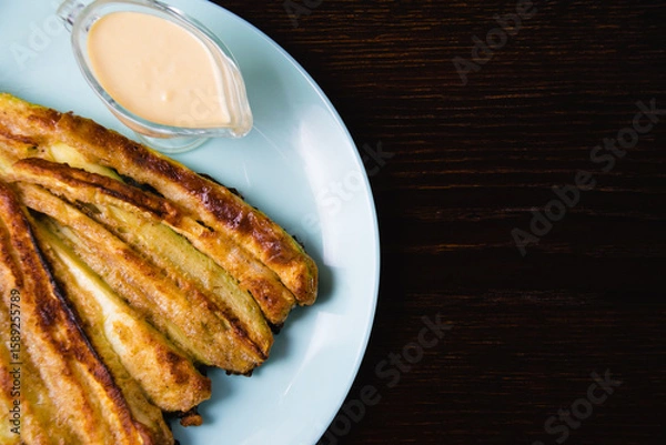 Fototapeta Delicious fried zucchini with aromatic sour cream garlic sauce on a plate on dark table