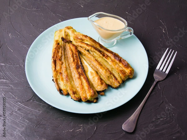 Fototapeta Delicious fried zucchini with aromatic sour cream garlic sauce on a plate on dark table