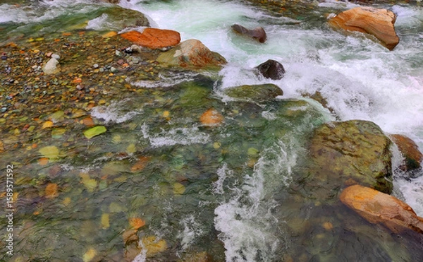 Fototapeta Top view of flowing river and stones. Vibrant river scene showcasing clear water rushing over colorful stones. Creating a dynamic and refreshing natural landscape.