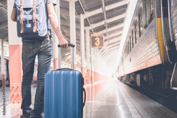 Fototapeta Enjoying travel. Young traveler walking with suitcase and classic train at railway platform. alone travel and summer concept. vintage filter.