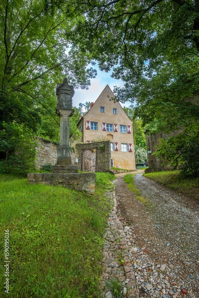 Obraz Historic building with half-timbered charm, surrounded by forest and nature, reached via an old cobblestone path with a stone gate and monument