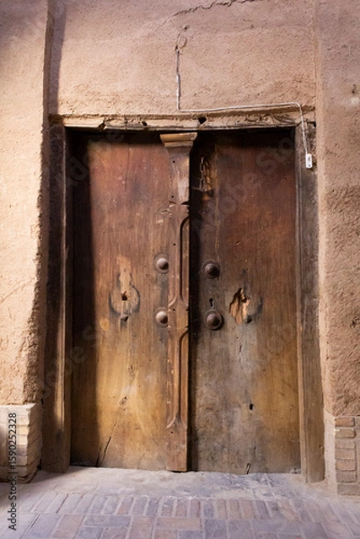 Fototapeta Weathered wooden door in Yazd, Iran, set in an earthen wall, showcasing traditional Persian architecture and timeless charm.