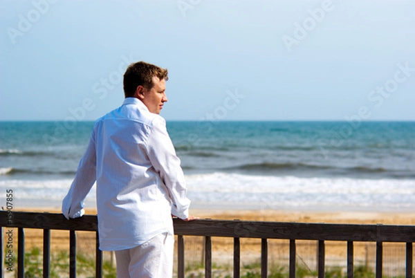 Fototapeta Young handsome man in white standing on a porch at the oceanfron