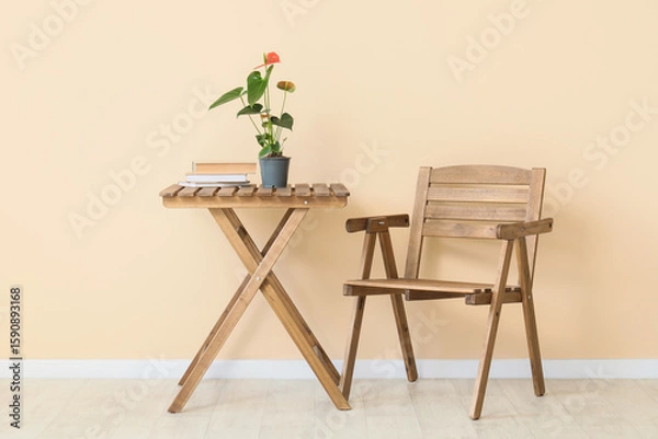 Fototapeta Beautiful Anthurium flower with books on table and chair near beige wall in room