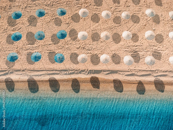 Fototapeta Aerial view of rows of beach umbrellas and deckchairs casting shadows on the sandy beach, by the turquoise sea