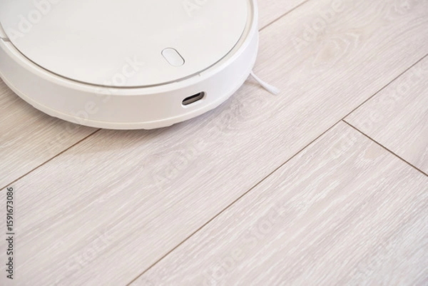 Fototapeta Modern white robotic vacuum on light wood floor in minimalist home setting for efficient cleaning.