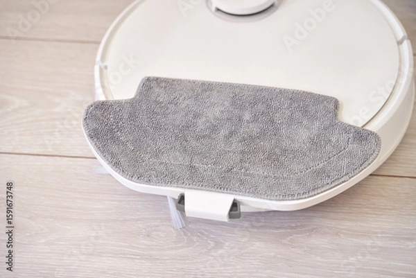 Fototapeta Robotic vacuum cleaner with attached mop on wooden floor for efficient home cleaning.