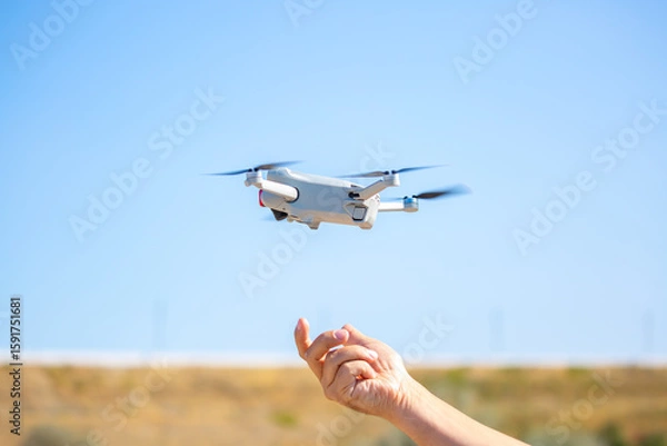 Obraz Quadcopter in flight against the sky. A small drone takes off from a person's hand.