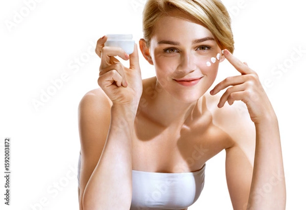 Obraz Beautiful woman applying moisturizer cream on her face. Photo of smiling woman with perfect skin on white background. Beauty concept