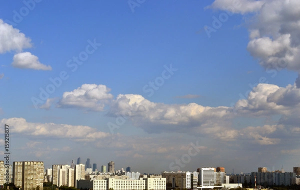 Fototapeta Fluffy clouds over the city in a clear sky