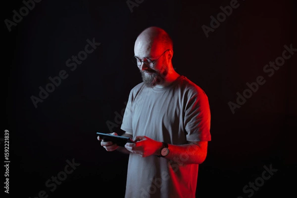 Fototapeta A focused man is using his smartphone against a dark background that features striking red lighting effects