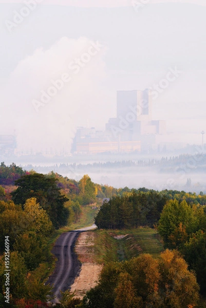 Fototapeta Misty Road Through Autumn Trees Towards Coal Power Plant in Foggy Background