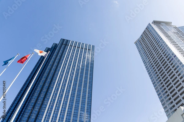 Obraz 青空にそびえる日本の高層オフィスビルと国旗｜ビジネス街・企業本社・グローバル経済イメージ