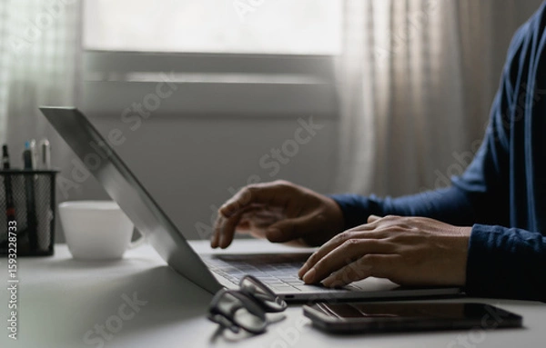 Fototapeta Close-up of man typing on laptop at home office, freelance work, online business, remote communication concept. Remote working, freelancer lifestyle, creative project, digital technology, modern work.