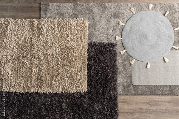 Fototapeta Top view of layered textured rugs in various neutral tones and materials, including circular tassel mat and fluffy pile carpets, arranged over wooden flooring in cozy minimalist decorative styling.
