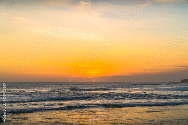 Fototapeta Sunset beach in Bali - Echo beach. Waves, tide and magic sea landscape view with a beautiful evening sky. Indonesia, Ocean. Orange beach pattern. Surfing Waves on the Tropical Beach. Panoramic Sunset