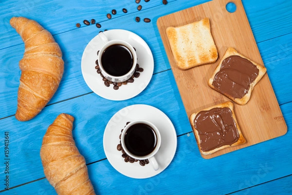 Obraz Two cups with coffee, croissant and toast with chocolate on a blue wooden table