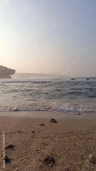 Obraz Peaceful coastal scene with sandy beach, waves, and distant cliffs under a clear sky