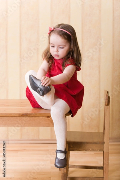 Fototapeta Little girl sitting on table and put on one's shoes