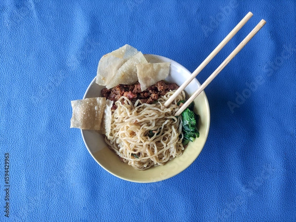 Fototapeta A bowl of chicken noodles with dumplings and green vegetables on a blue tablecloth