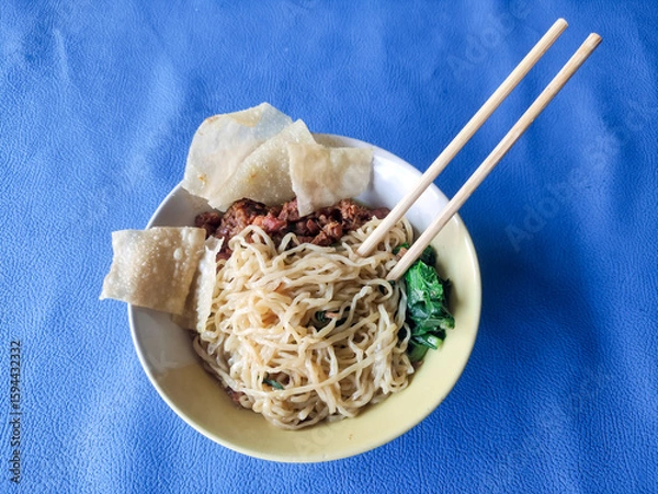 Fototapeta A bowl of chicken noodles with dumplings and green vegetables on a blue tablecloth