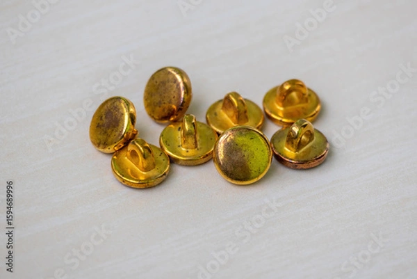 Fototapeta Vintage golden buttons on a wooden surface, ideal for fashion, craft, and antique themes. Perfect for designs needing a touch of old-world charm and decorative texture.