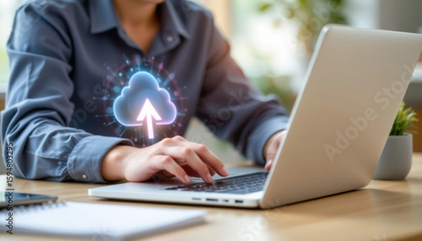 Obraz A person using a laptop with a cloud upload graphic, symbolizing digital storage and data management in a modern workspace.