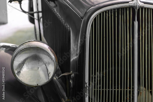Fototapeta headlight and radiator grille of a vintage car. Classic design with vertical chrome slats and black bodywork.