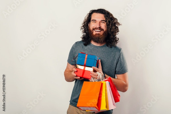 Obraz A cheerful man joyfully holds colorful gifts and bags while celebrating his delightful shopping experience