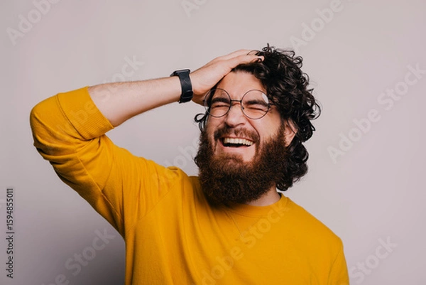 Obraz A man with curly hair and a beard in a vibrant yellow sweater shows a mix of frustration and a smile
