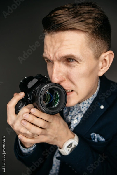 Obraz Portrait of a young photographer with a camera in his hands, with a nervous expression on his face. Studio shot